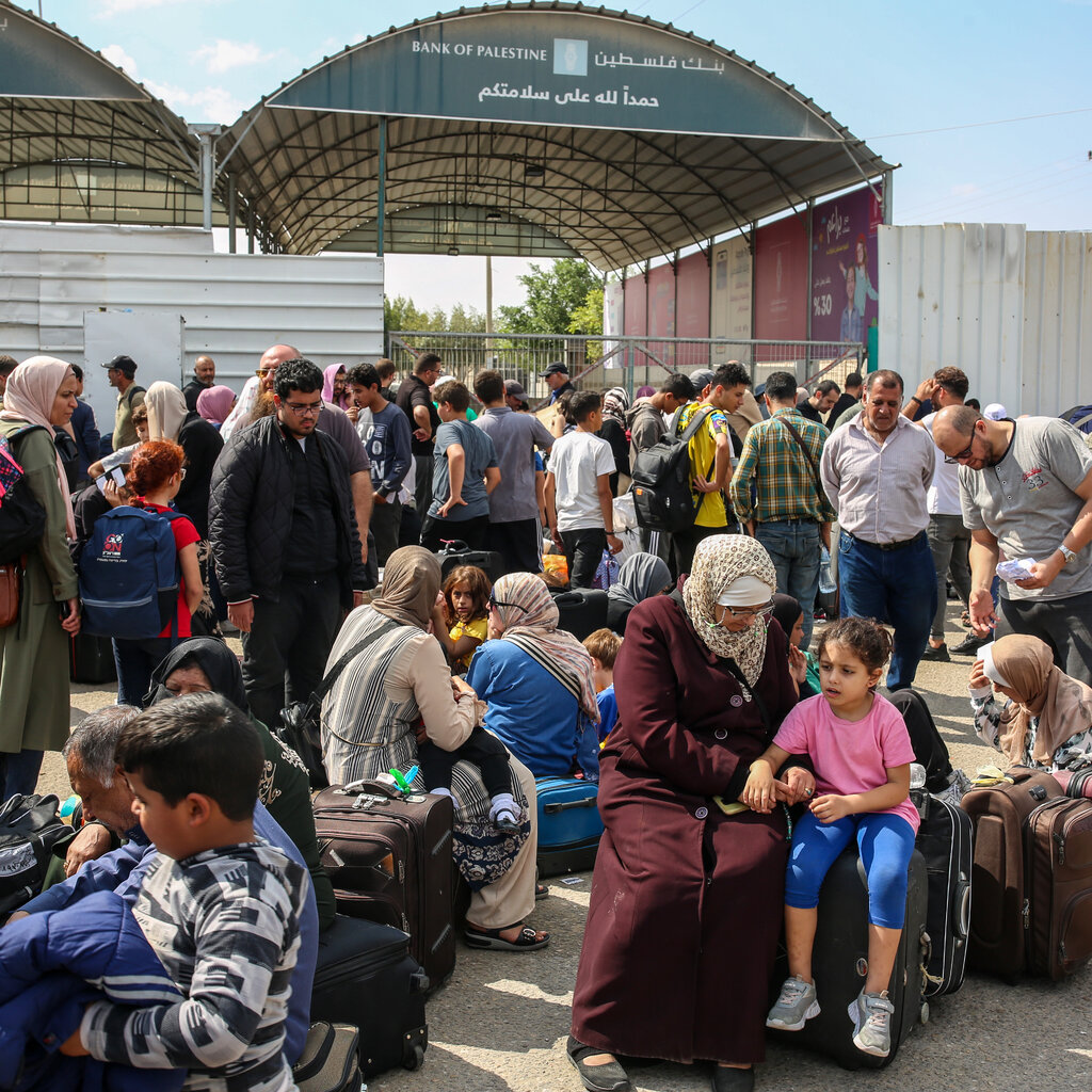 People standing and sitting among suitcases in front of a border gate. 