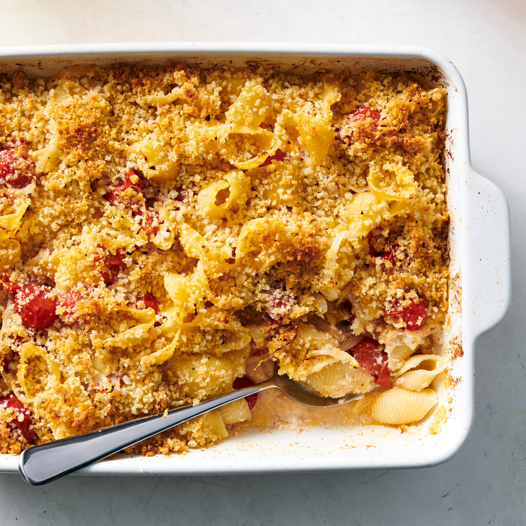 A white ceramic dish holds a ricotta pasta bake showered with golden bread crumbs.