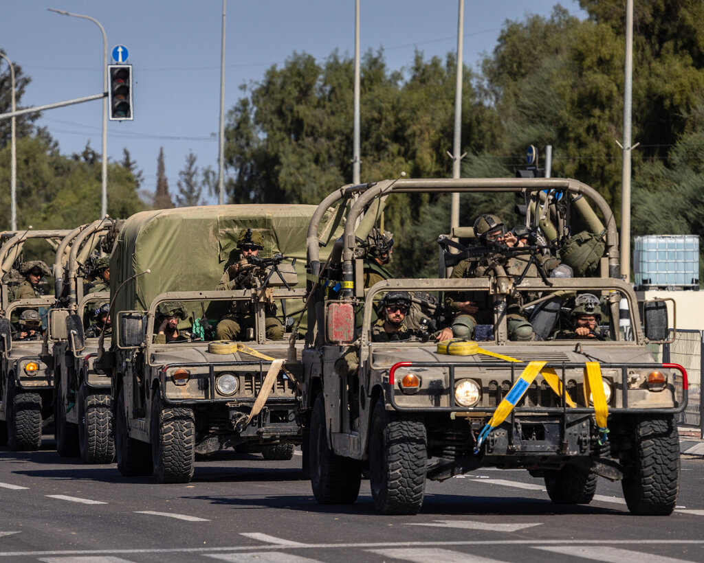 Military vehicles filled with soldiers driving in a line on a road.