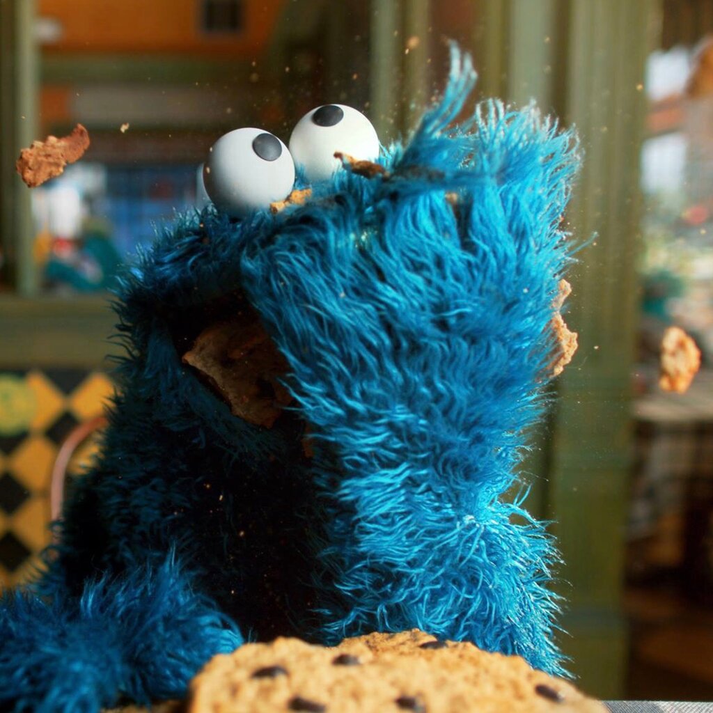 A blue muppet, the Cookie Monster of “Sesame Street,” with a giant cookie.