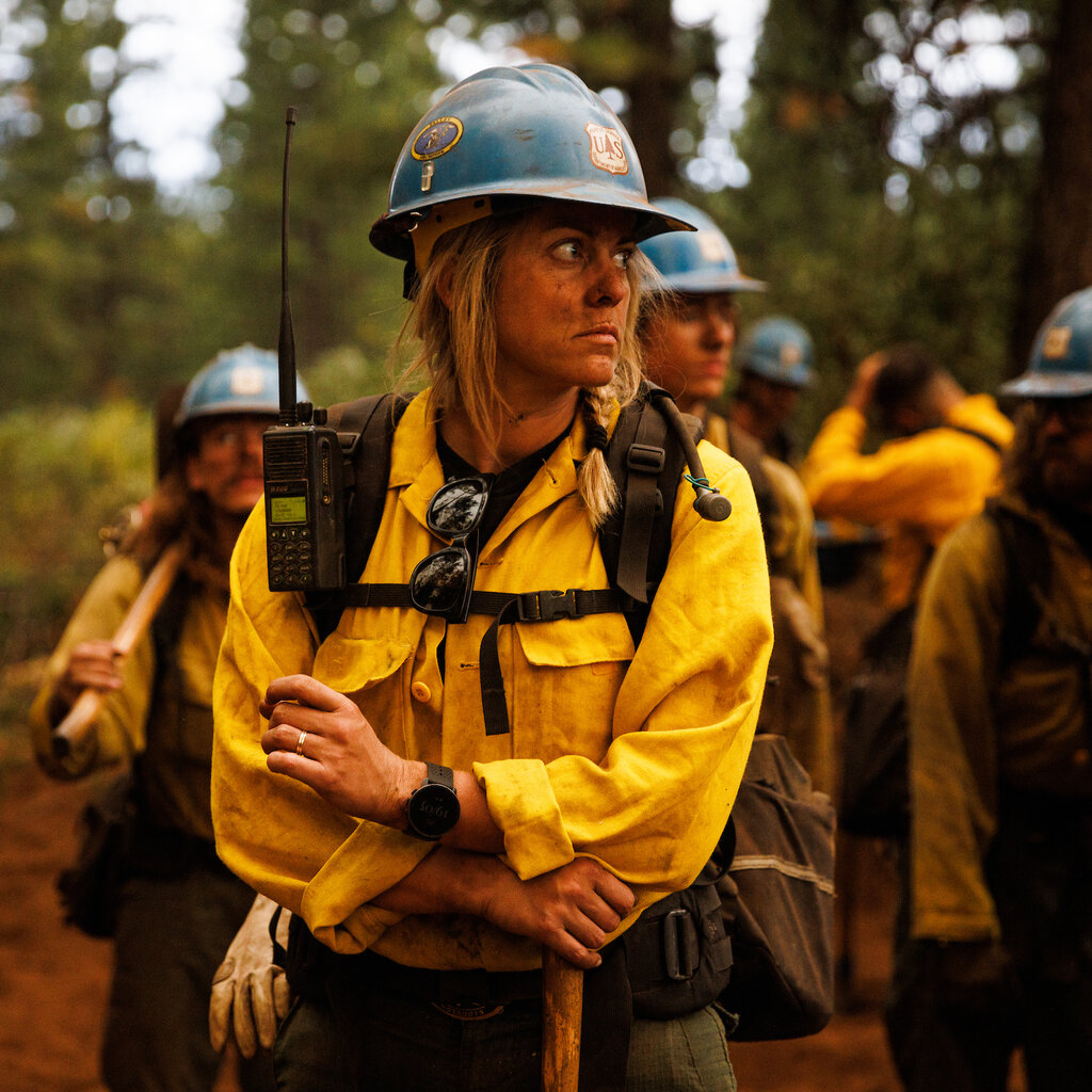 A firefighter in a yellow shirt and blue helmet stares into the distance.