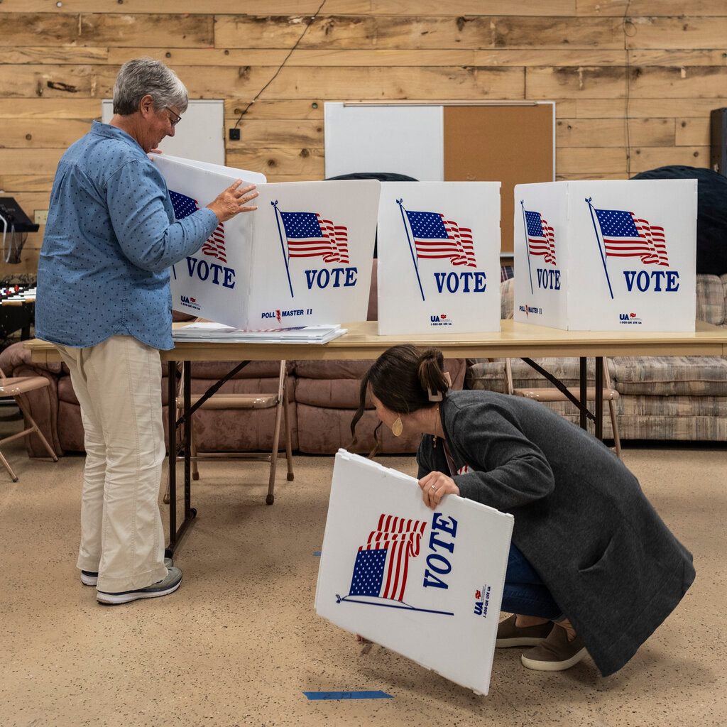 Election officials taking down a polling site in Iowa this month. A table has several white placards with “vote” written on them next to depictions of the American flag.