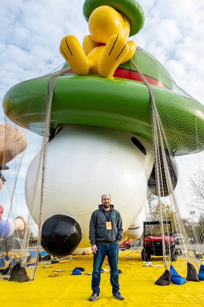 The inflated head of a giant Snoopy balloon sits under netting, with a man in a gray sweatshirt standing in front.