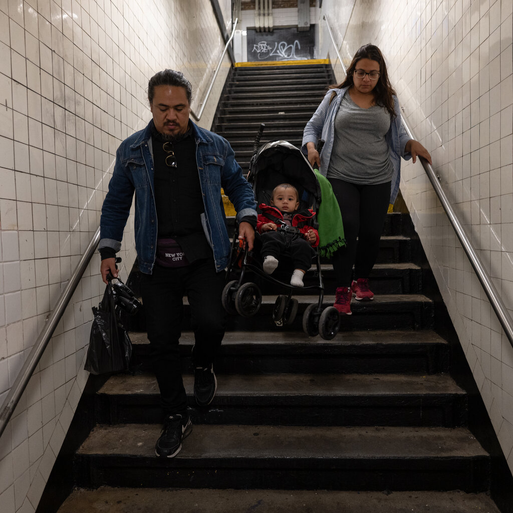 A man and woman carry a baby in a stroller down a flight of stairs. 