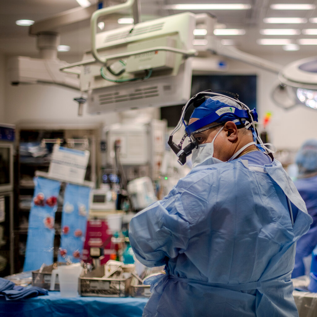 A doctor in blue scrubs and blue head gear in the foreground of a surgery unit.