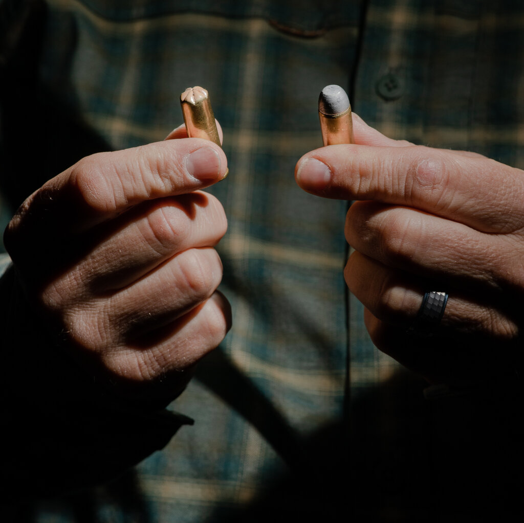 Close up of two hands; the left holds a blank; the right holds a dummy round.