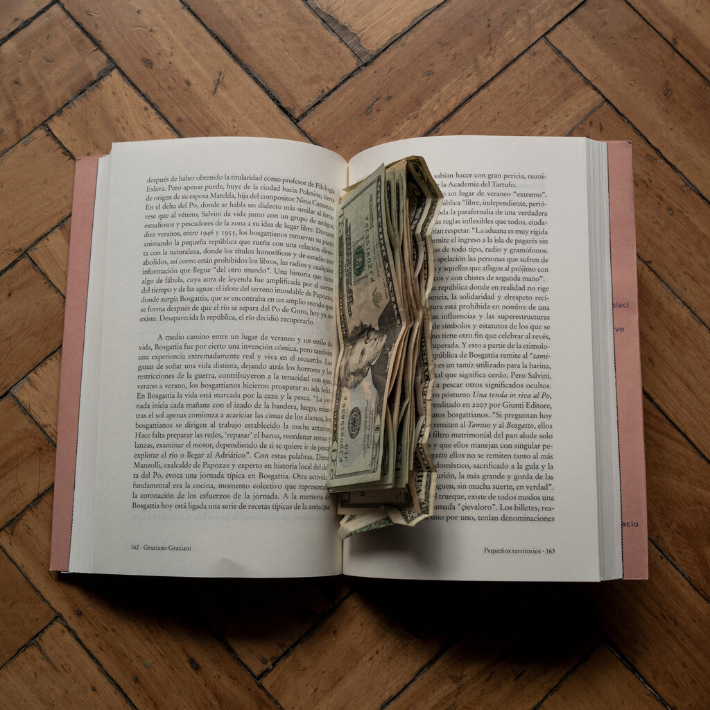 An open book with a dollar bills stuffed in its seam. 