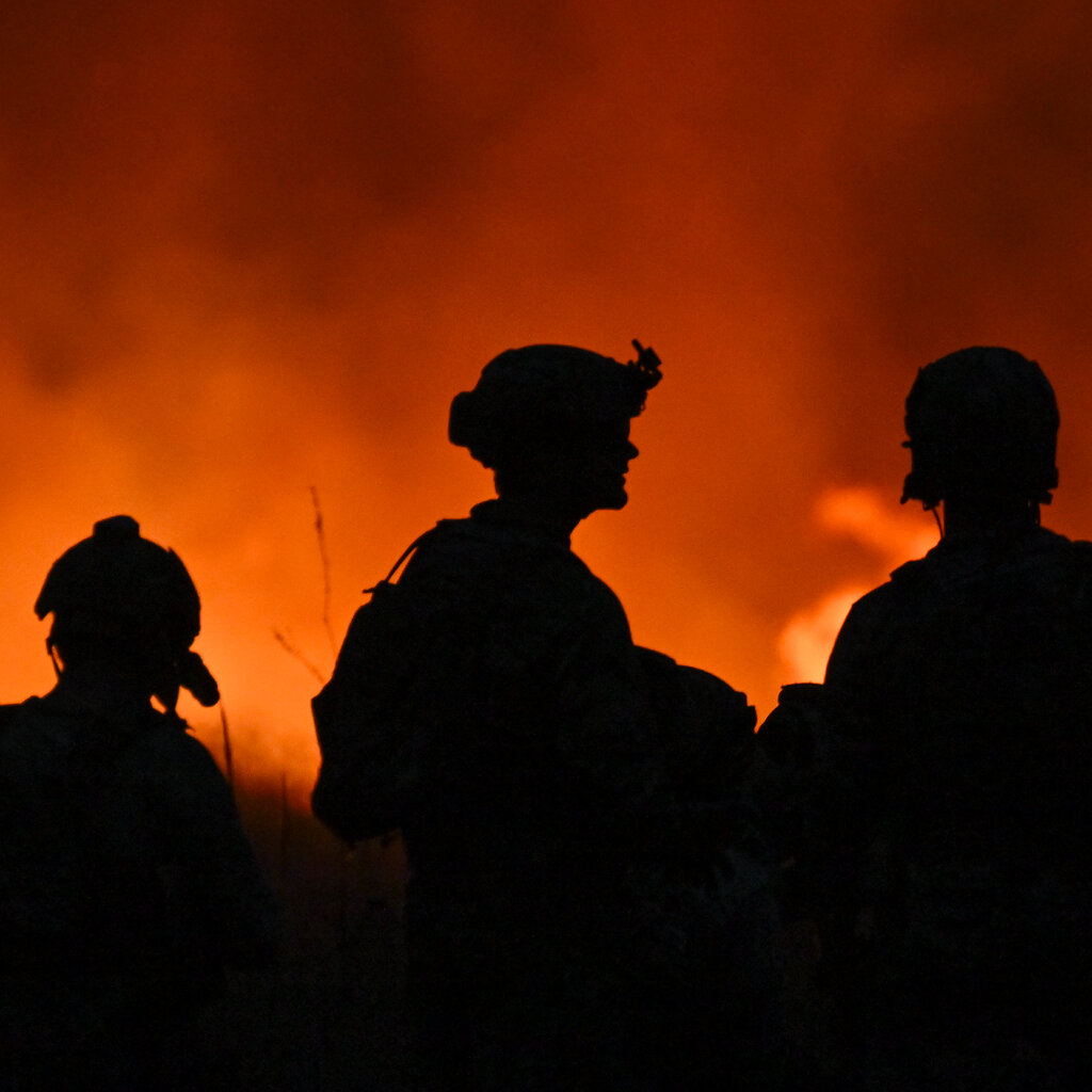 Three silhouetted soldiers stand before a fiery orange backdrop.