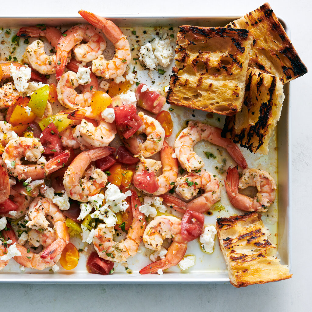 A sheet pan with slices of bread, shrimp, tomatoes and feta topped oregano.
