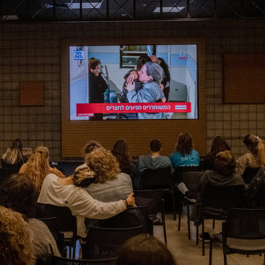 People sitting in a room watching a projection of a news broadcast.