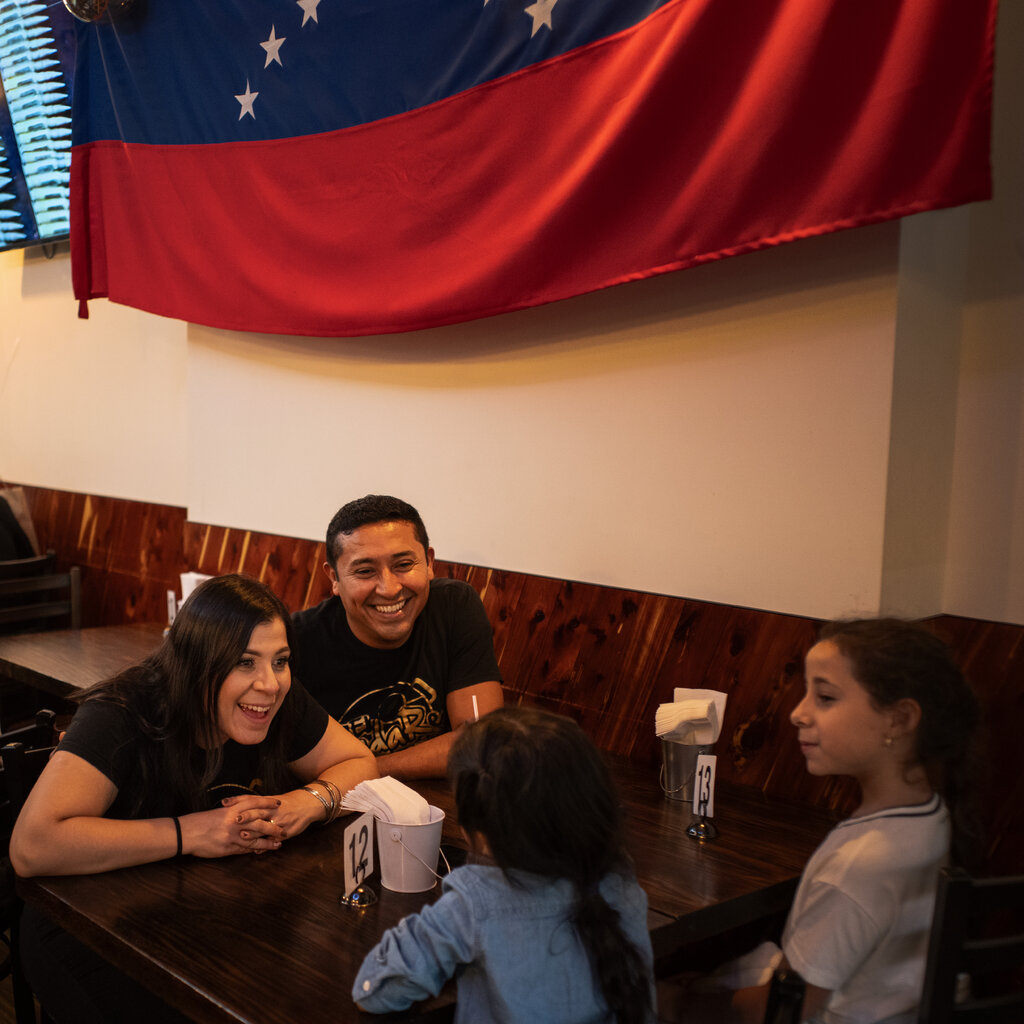 Sandra Sayago and her husband, Alfredo Herrero, sit at a table at their restaurant, El Budare Cafe, facing two young girls. 