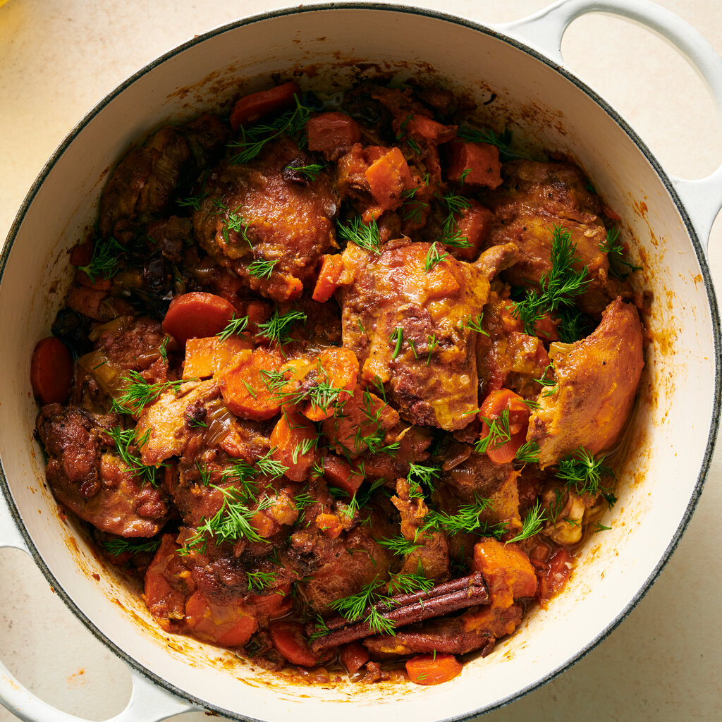 A white, cast-iron Dutch oven holds braised chicken thighs with sweet potatoes and dates.