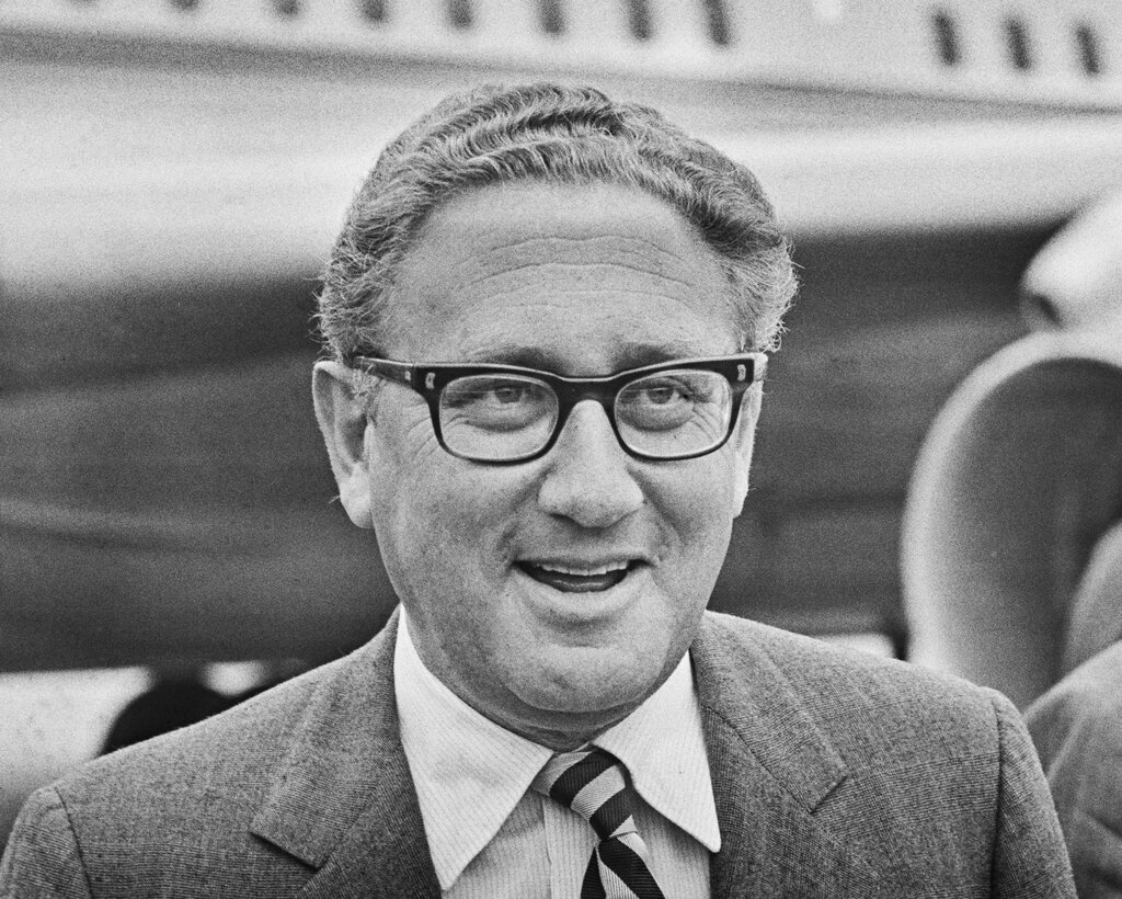 Henry Kissinger in glasses, a suit and a striped tie. 