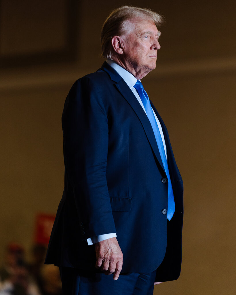 Donald Trump stands wearing a suit and blue tie.