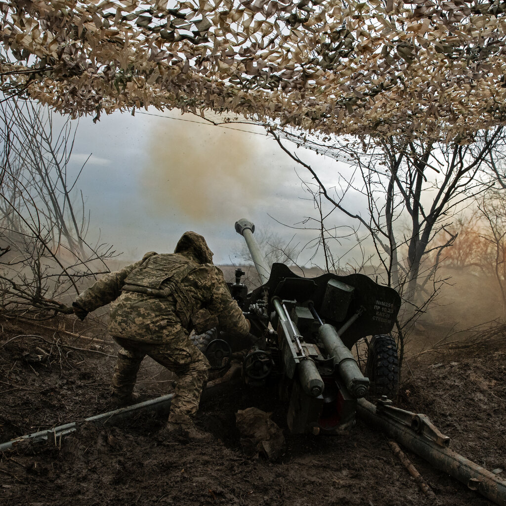 Ukrainian soldiers in fatigues and under a camouflaged covering firing at Russian positions.