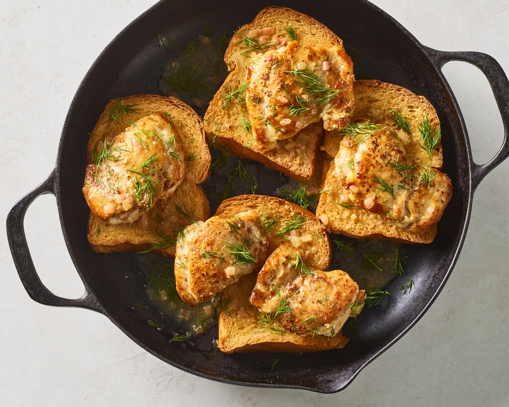 Four pieces of brioche are topped with chicken and herbs in a buttery pan sauce in a skillet.