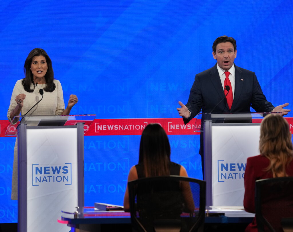 Nikki Haley in a white dress and Gov. Ron DeSantis in a suit and red tie speak simultaneously during the fourth Republican presidential primary debate.
