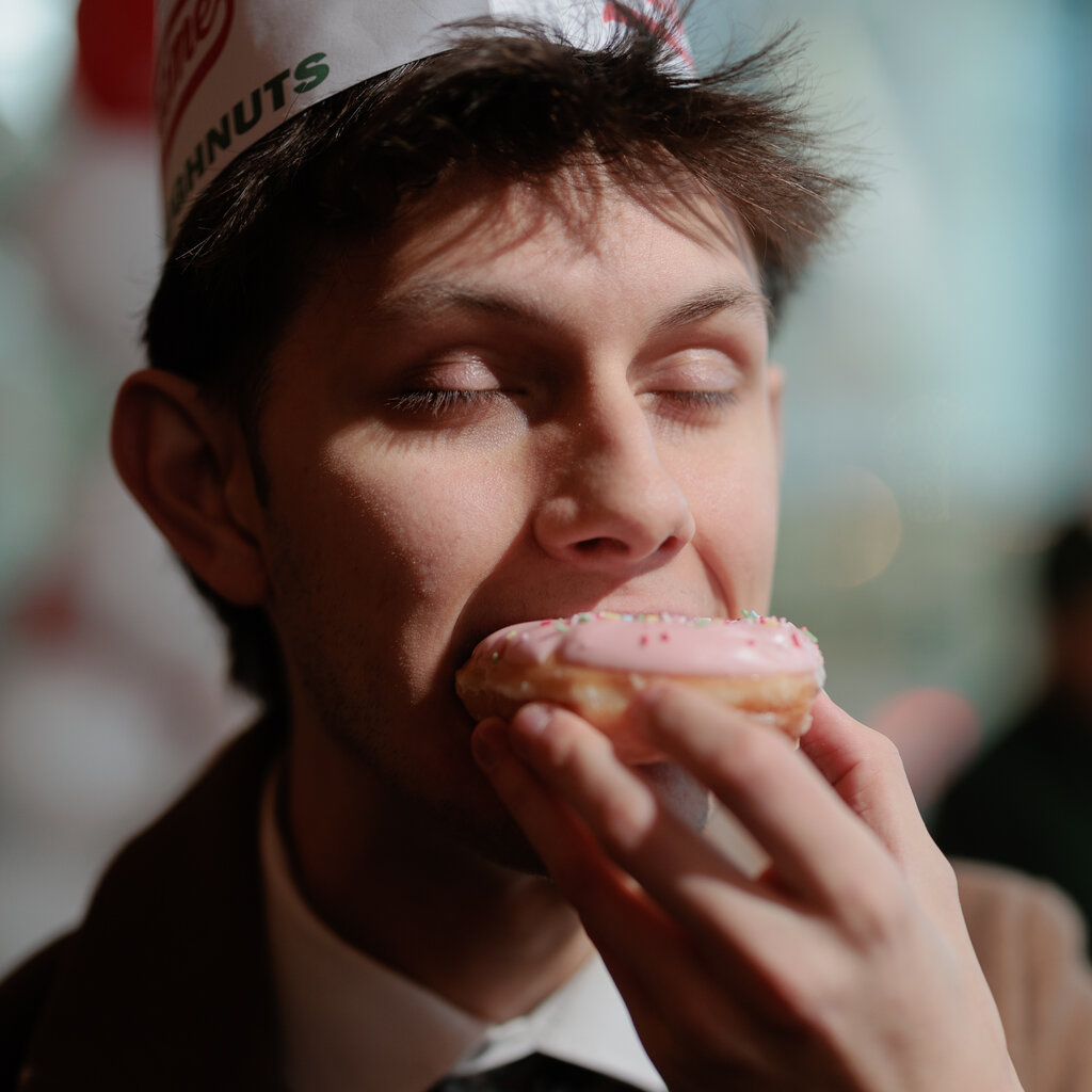 A customer eats a pink, sprinkled doughnut. 
