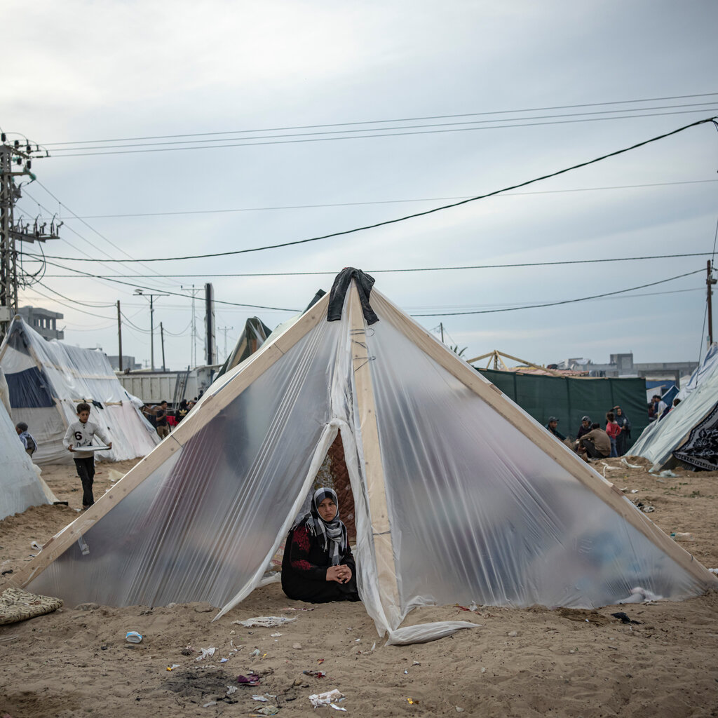 A woman sits inside a makeshift plastic tent, which is supported with two-by-fours. 