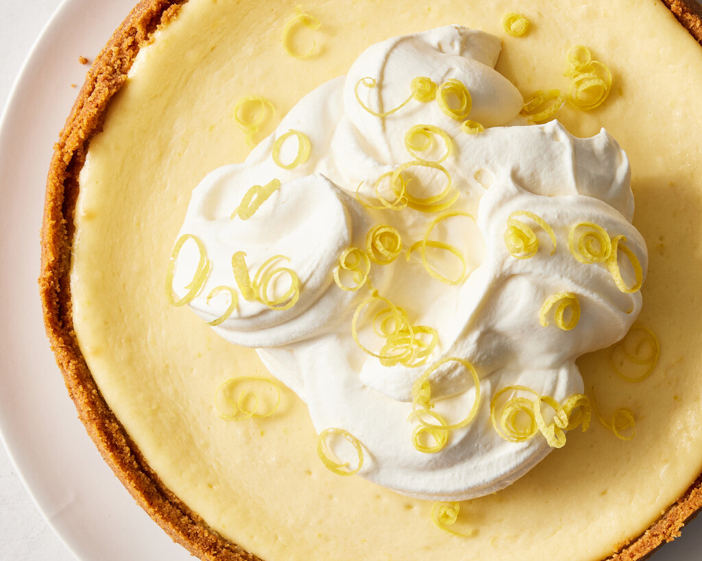 A pie with yellow filling, topped with whipped cream and garnished with lemon zest. 