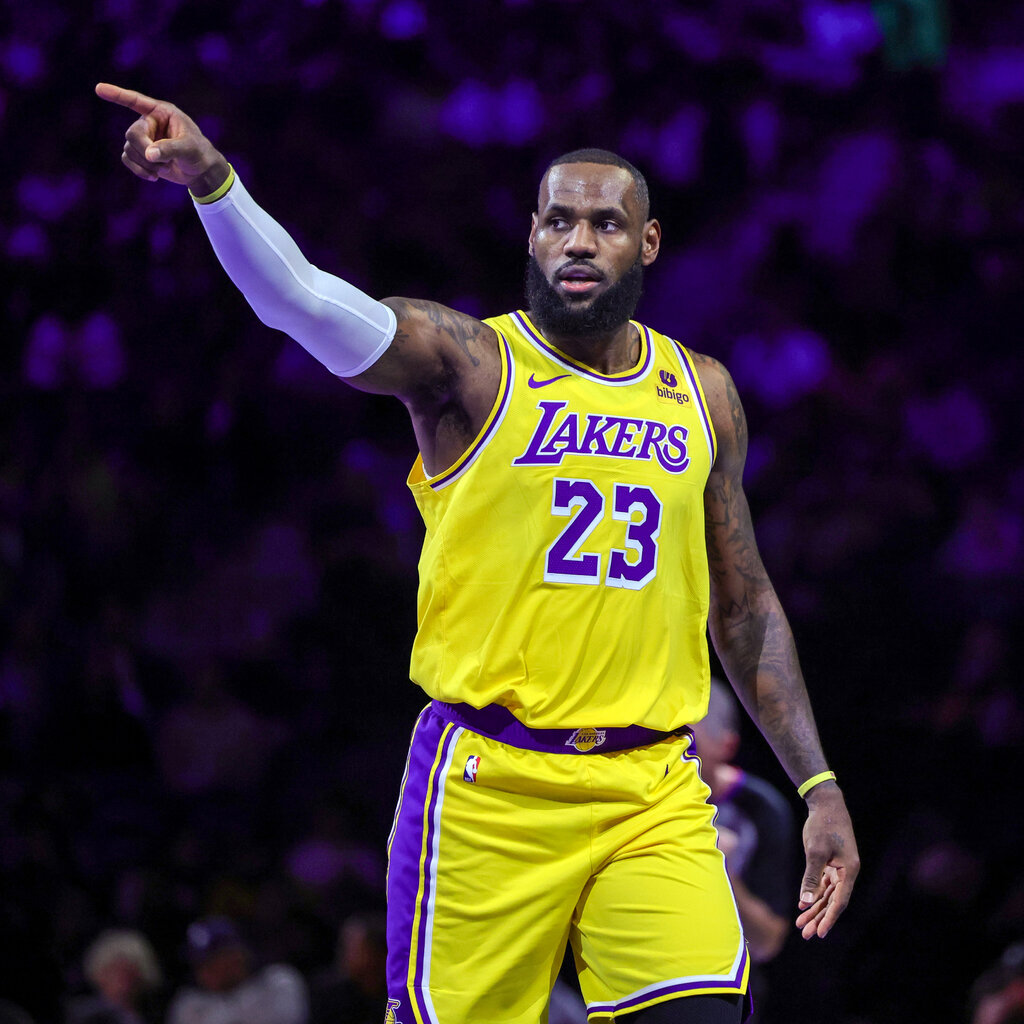 Lebron James, wearing a yellow and purple basketball jersey, points a finger in the air.