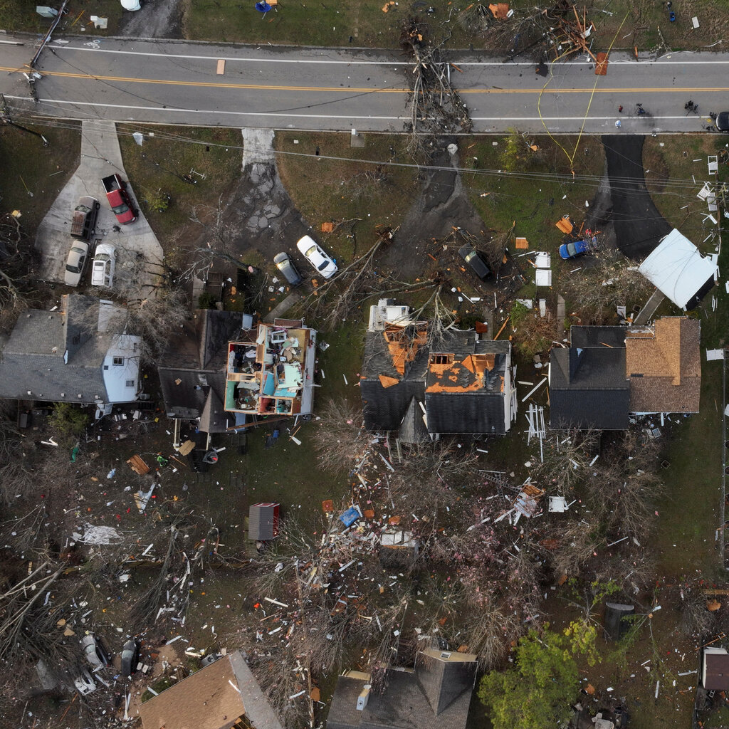 An aerial view of damaged homes, with debris scattered on the ground off a two-lane road. 