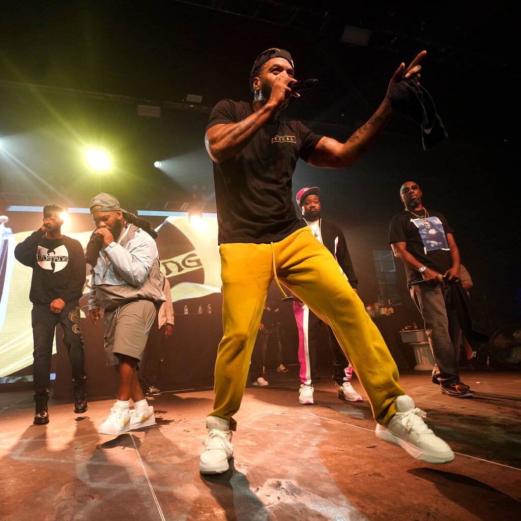 Members of Wu-Tang Clan singing and dancing with microphones in their hands and a bright light shining down.