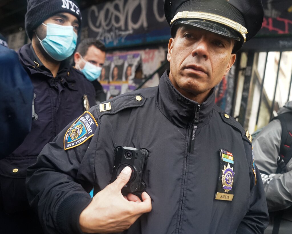 A police officer in a hat and uniform presses a button on his body camera.
