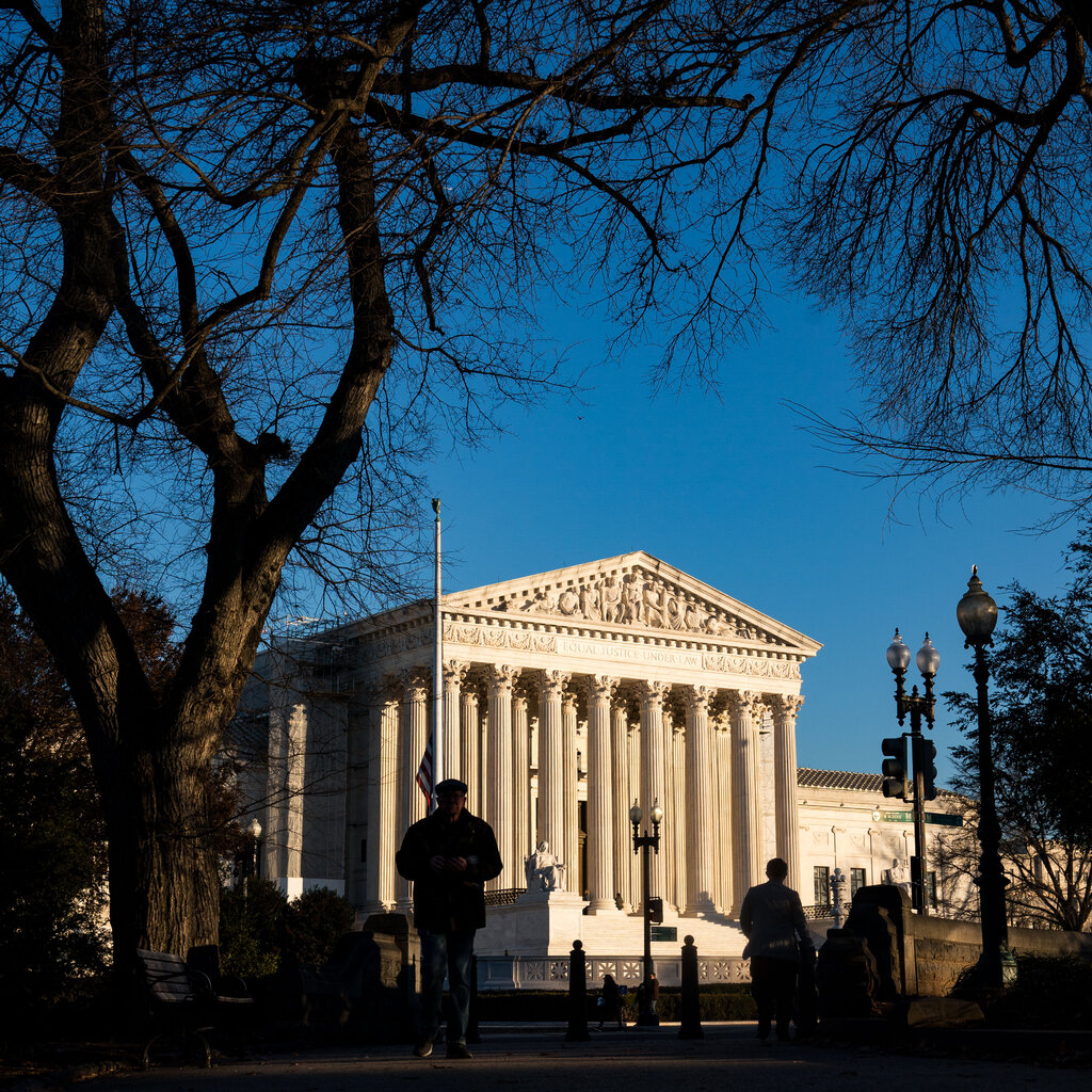 An exterior view of the U.S. Supreme Court building in Washington under a blue sky, with pedestrians and bare trees in the foreground.