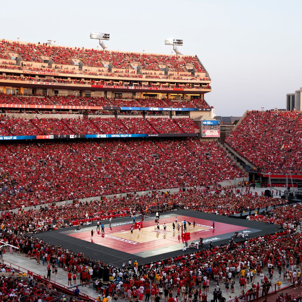 A large outdoor stadium full of fans wearing red watching a volleyball match.