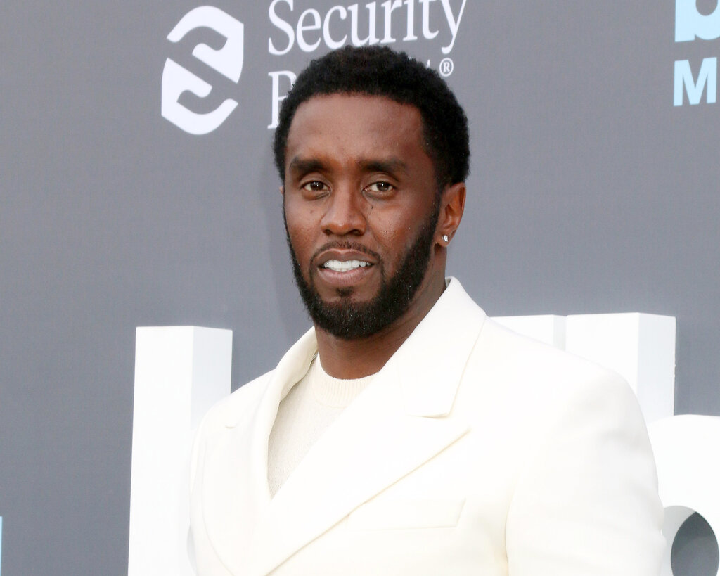 Sean Combs in a white suit and shirt, looks at the camera.