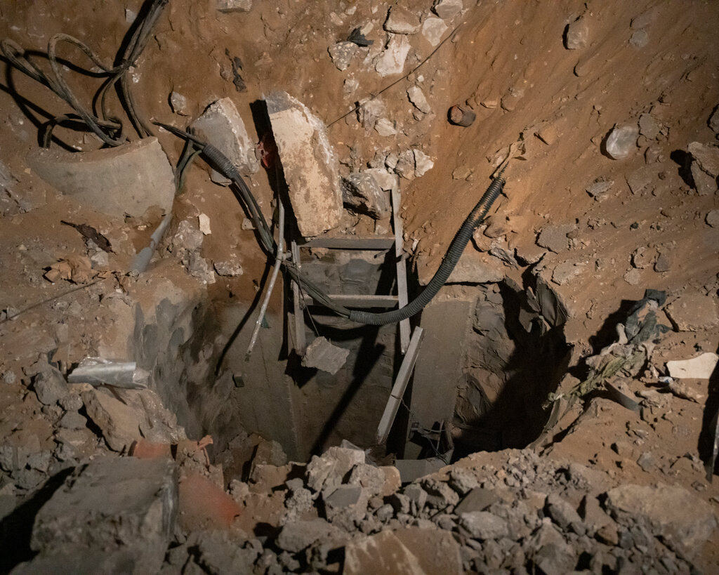 A hole in the ground surrounded by dirt and stones. Cords and metal pieces poke out in the area.