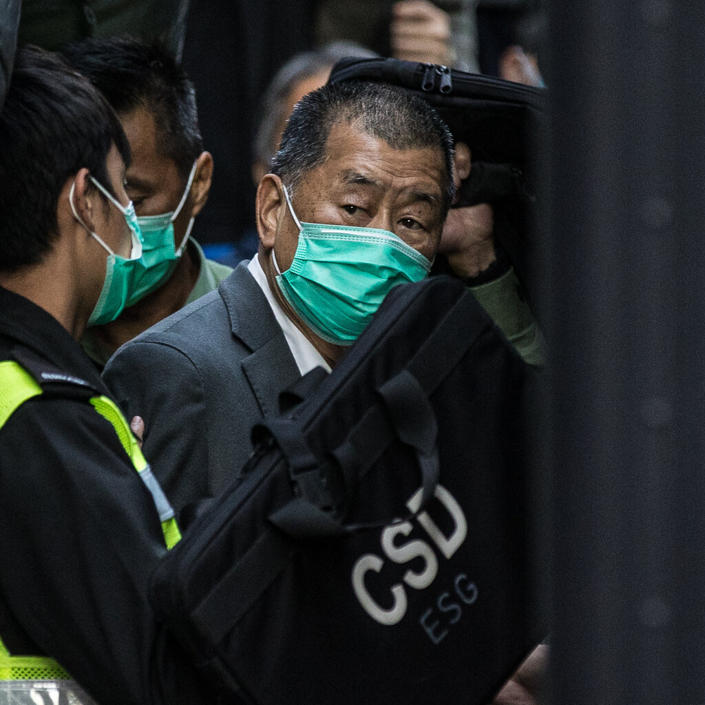 Jimmy Lai amid a crowd, wearing a mask and a gray suit. 