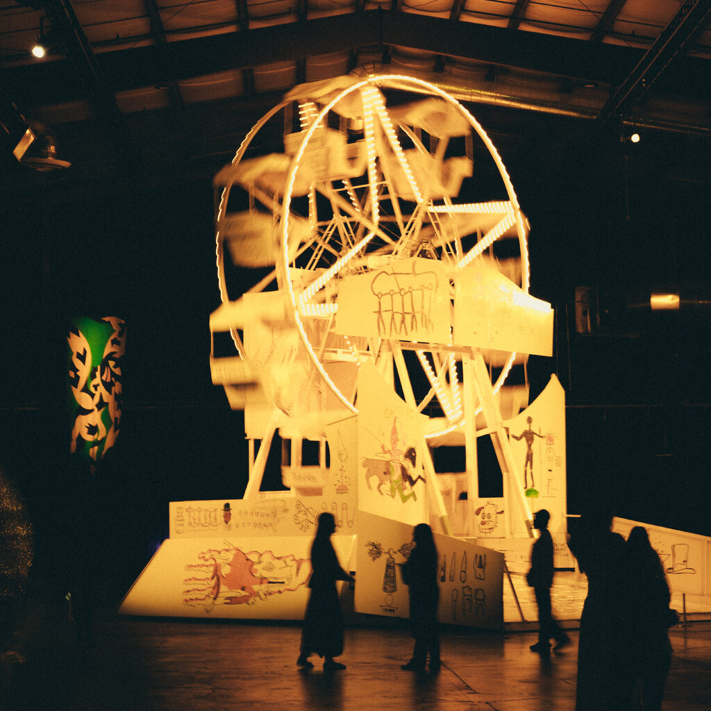 A small ferris wheel lighted up in a dark warehouse. 
