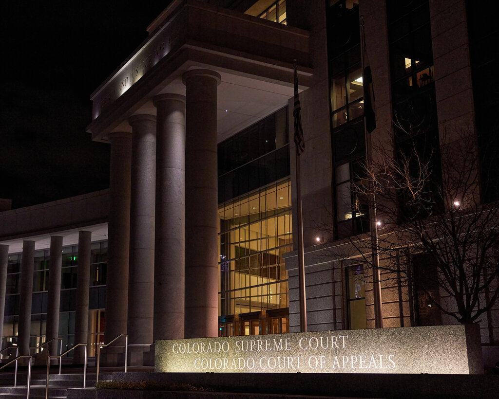 A stone-columned courthouse at night with lights on a sign that reads Colorado Supreme Court and Colorado Court of Appeals.
