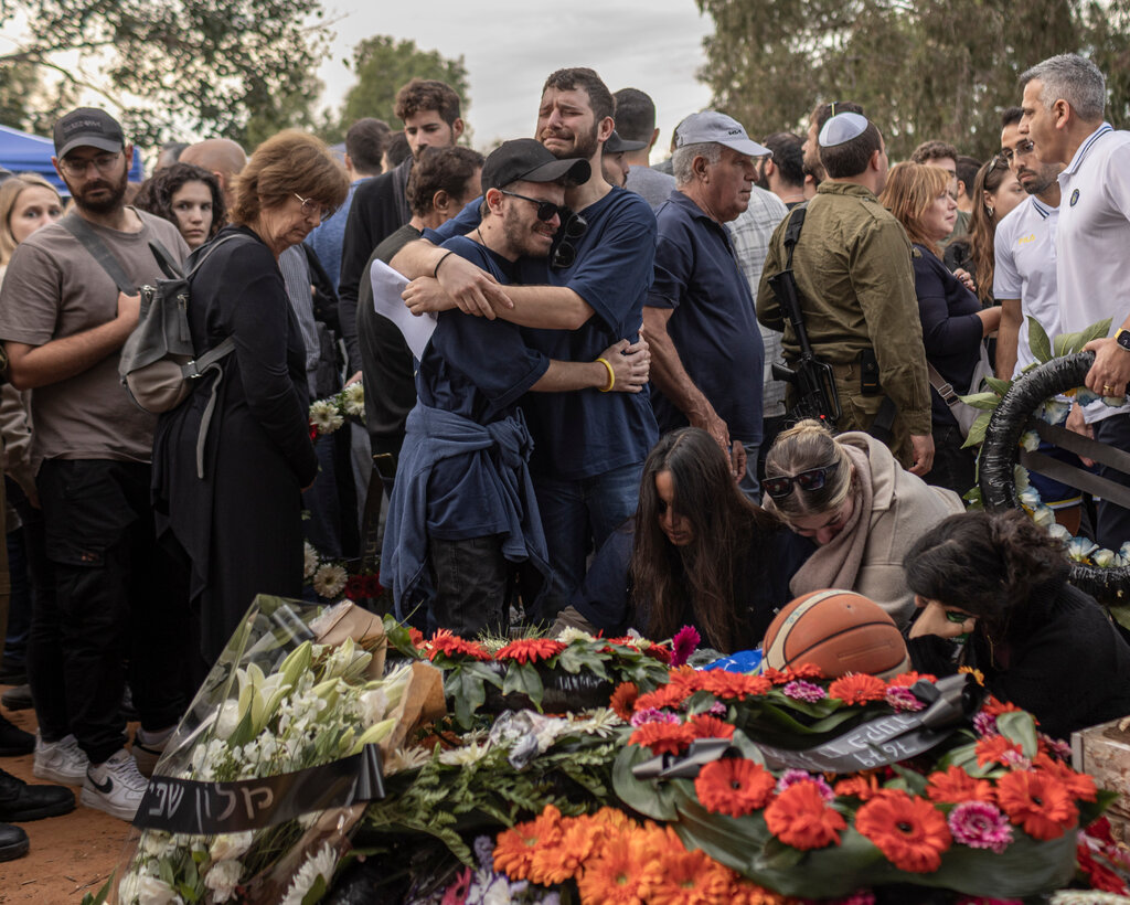 Two people embrace as others stand around them at a funeral.