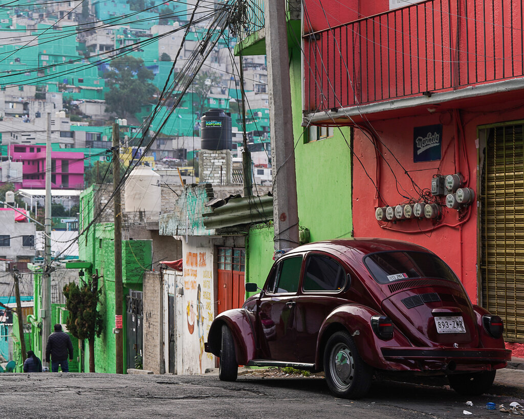 A maroon Beetle parked on a side street at the top of a hill. 