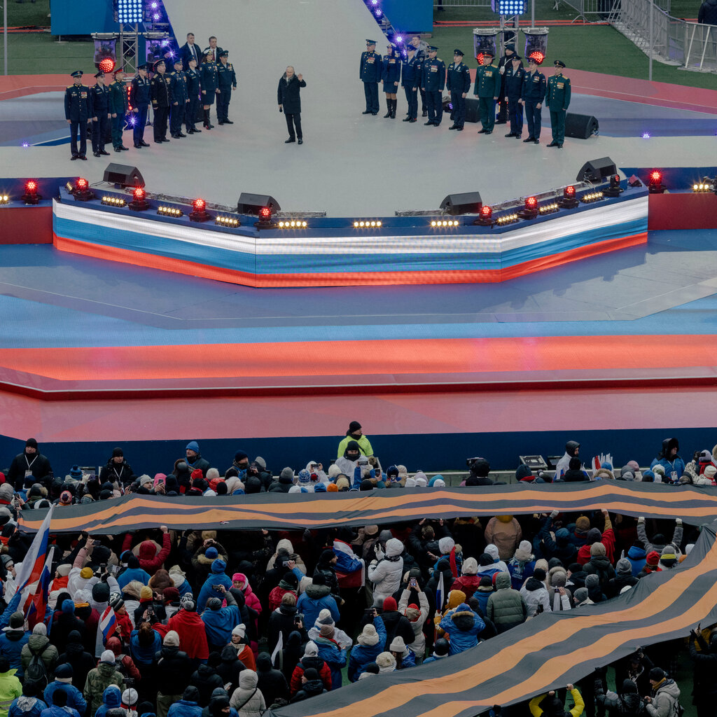 President Vladimir V. Putin of Russia speaks onstage at a rally. Members of the military flank him.
