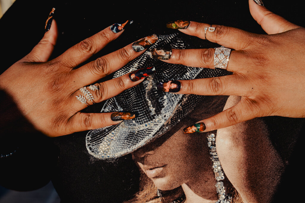 Two hands with sparkly rings and nails adorned with images of Beyoncé. The hands are lying flat on a black shirt featuring an image of Beyoncé.