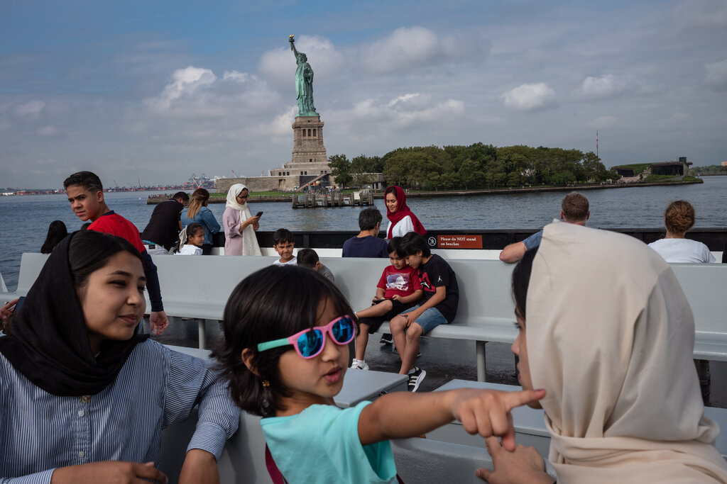 Passengers on a ferry passing by the Statue of Liberty. In the foreground are a child and two women wearing head scarves.
