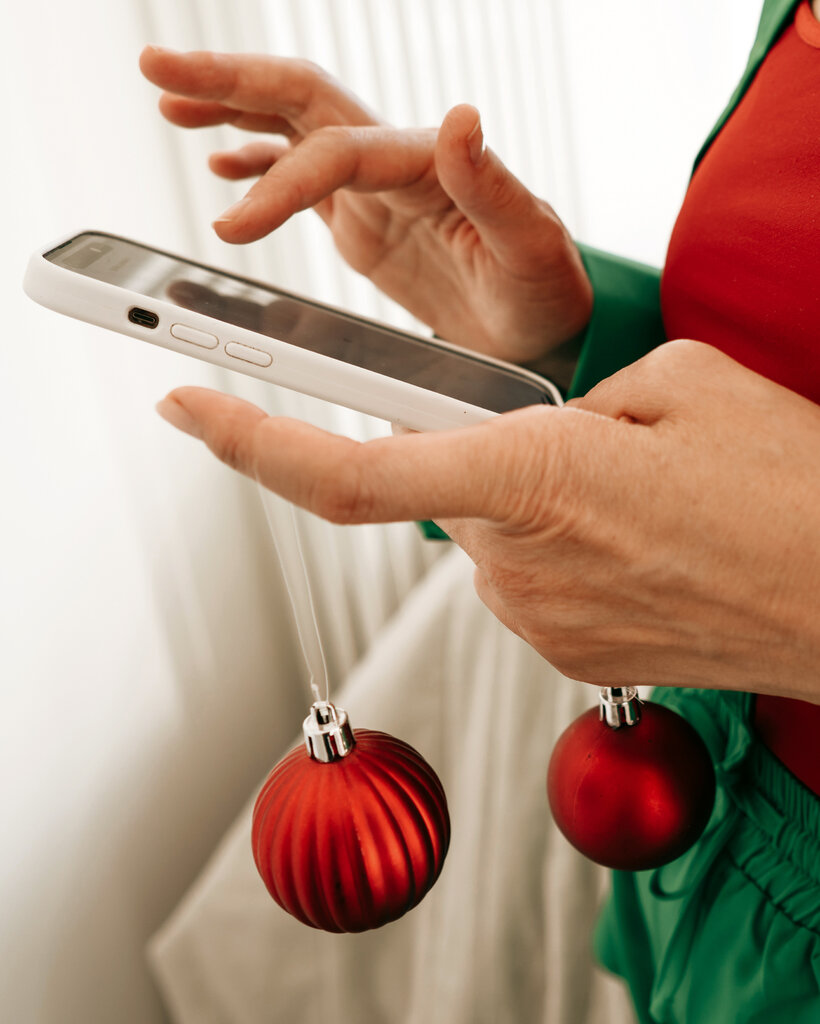 A person holding a mobile phone and red ornaments dressed in a green holiday suit.