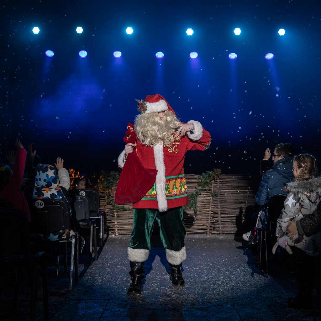 A man dressed as Santa Claus, holding a sack, walks down an aisle during an event. 