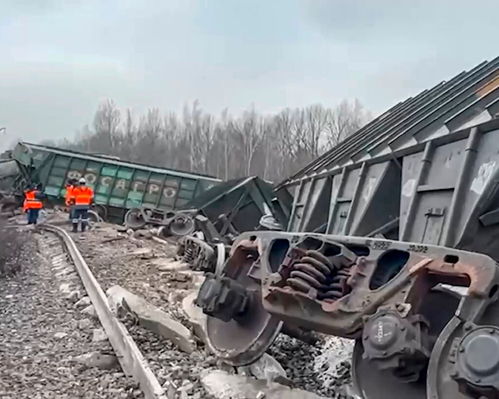 Railway workers standing on the tracks next to derailed train cars.