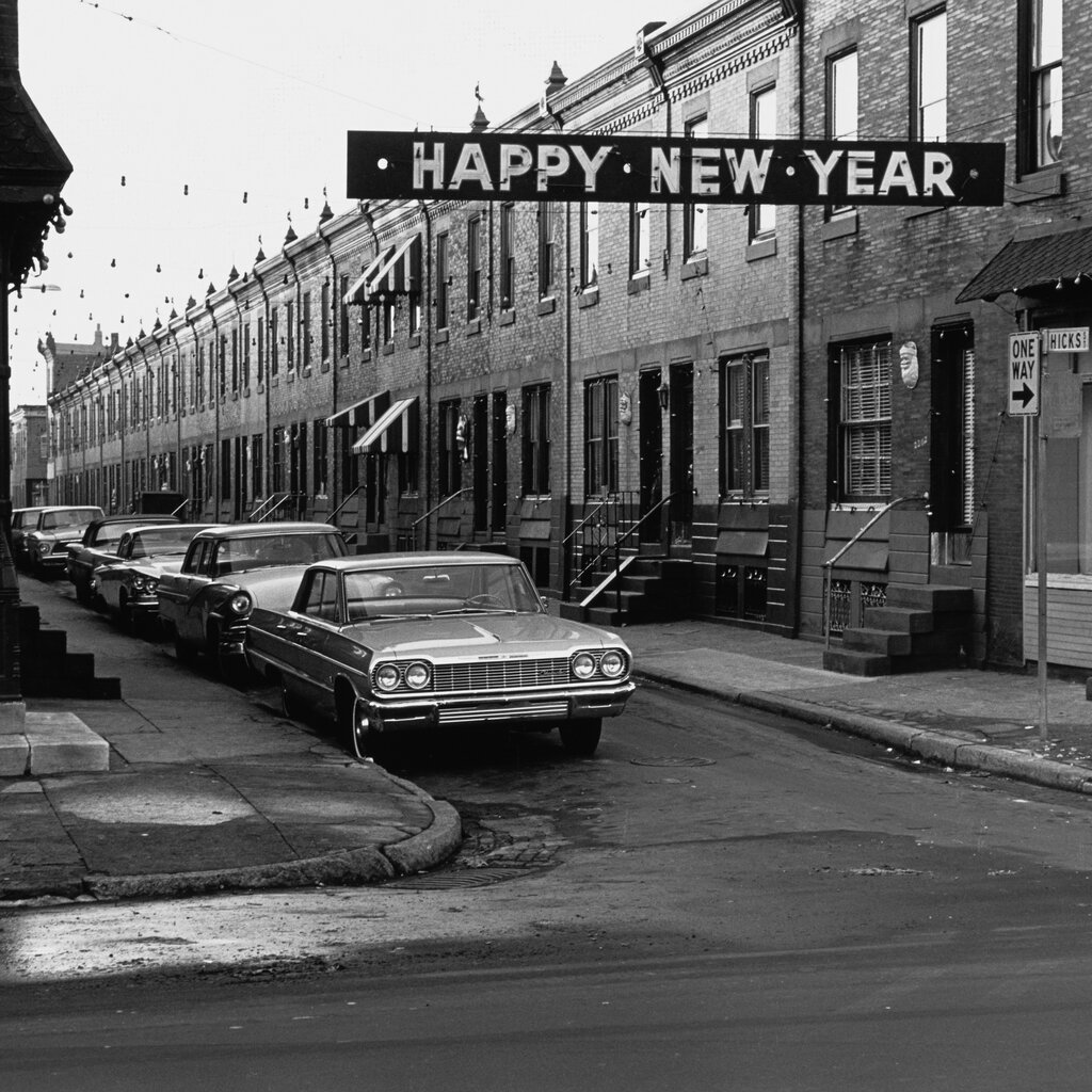 A banner on a street reads “happy new year.” Cars also line the street. 