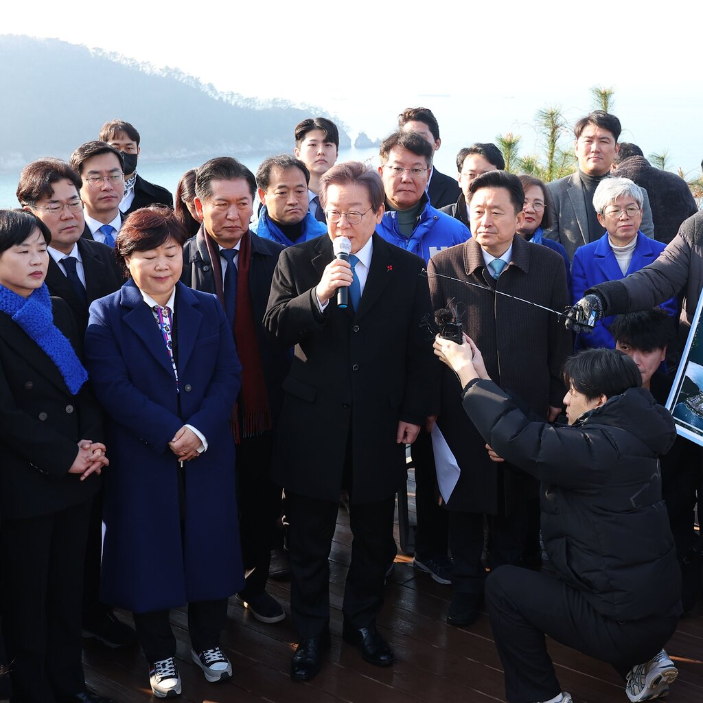 A man in a suit surrounded by people speaks during a visit to the construction site of an airport.