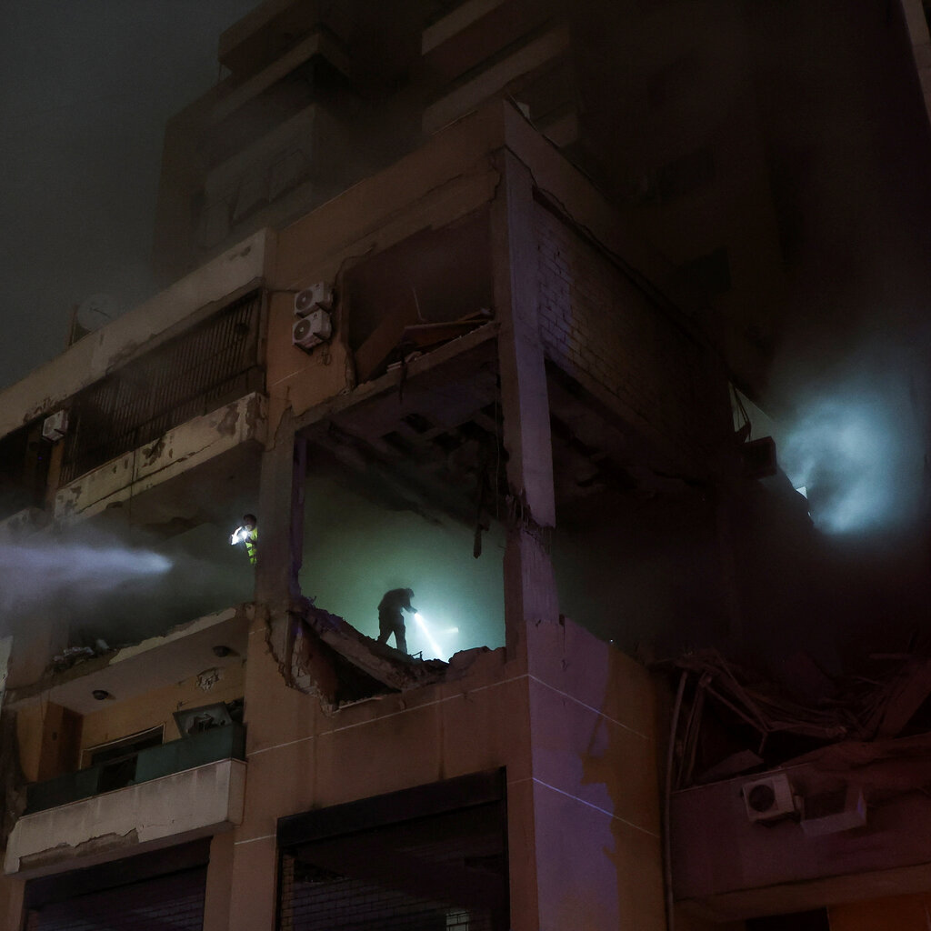 A building with the walls destroyed is filled with smoke. In the smoke is the silhouette of a person holding a flashlight and illuminating the room.