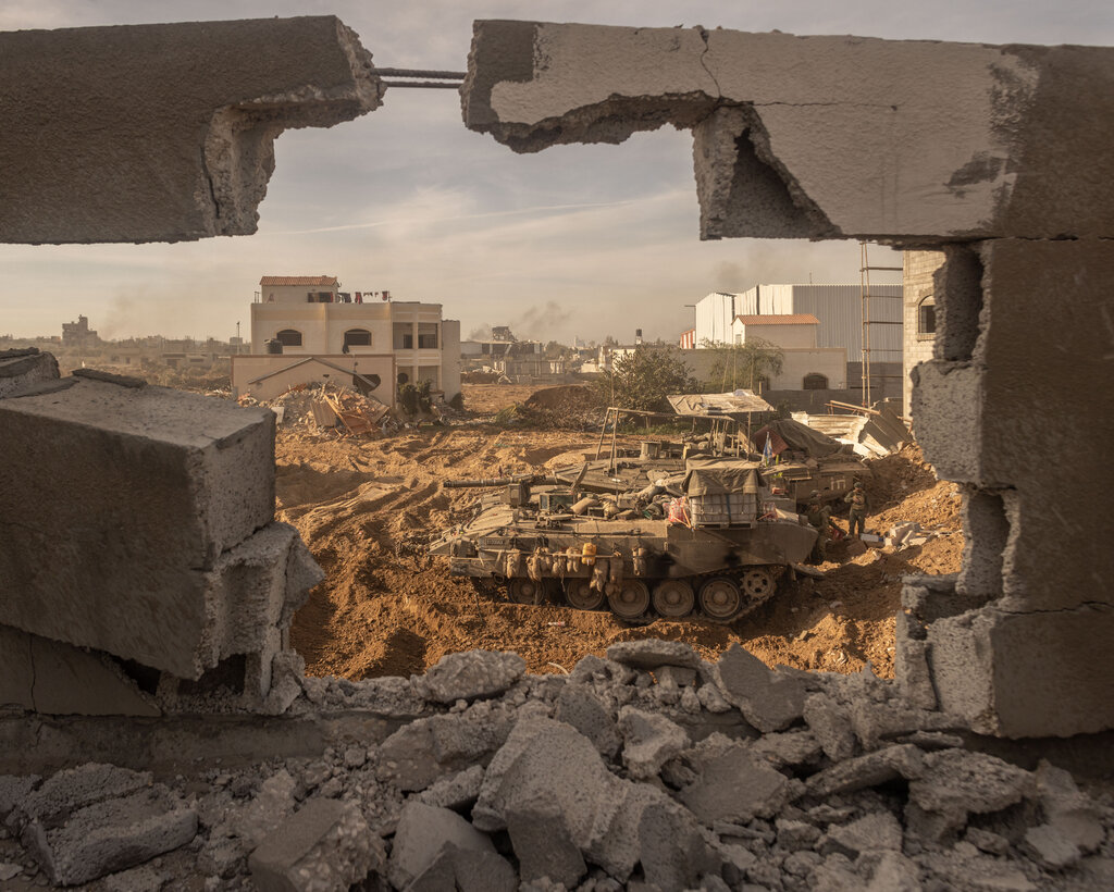In the foreground a destroyed wall frames a tank rolling through a dirt path.