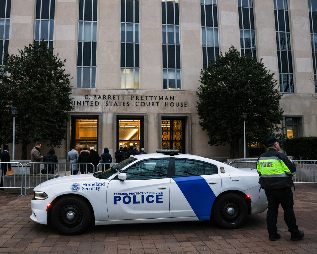 A police car and police officer in front of barriers and a line of people outside of a courthouse in Washington.