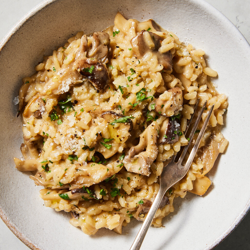 A plate of mushroom risotto, with green herbs and cheese on top. 