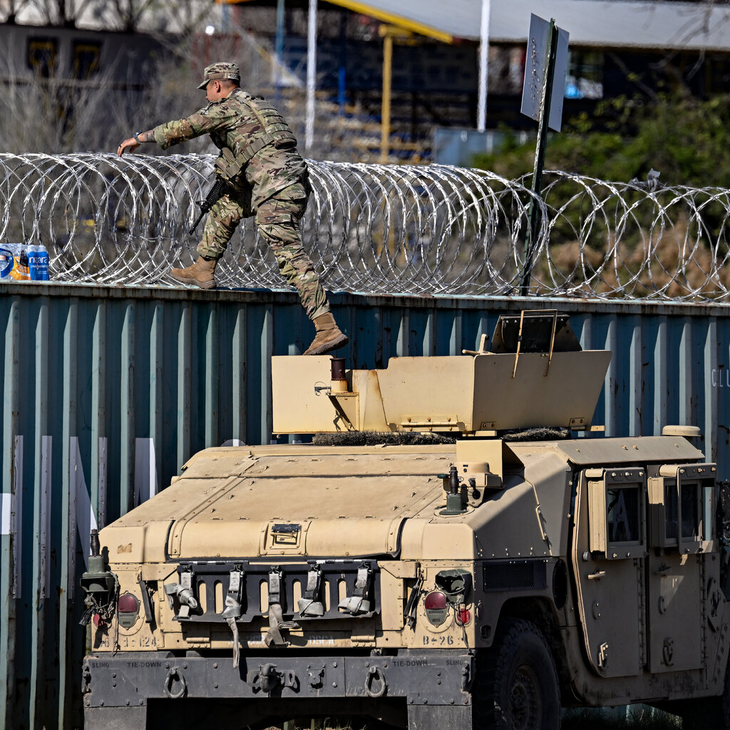 A member of the National Guard stepping off a vehicle near barbed wire.
